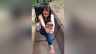 Beautiful Teen In Jeans Sitting On The Bench Outdoors Playing With Her Feet