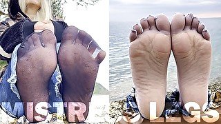 Feet tease in black and grey nylon socks wiggling toes at the seashore