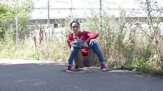 Cute nerdy brunette in sweatshirt and sneakers pisses on the road