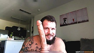 Tattooed solo guy spreads his legs to ride a massive dildo at home