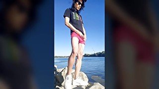 Twink boy with long dark hair pissing pee on the river dressed in glasses cap sneakers boxer tshirt