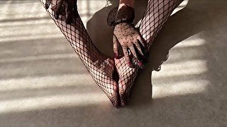 The girl caresses her legs in fishnet tights and strokes them with her hands in lace gloves