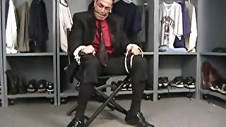 SUG Tuxedo clad man tied to chair ball gagged and struggling.