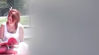 Gorgeous redhead is secretly recorded while she reads a book in the park.