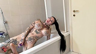 Tattooed girl with big boobs strips in the bathtub and masturbates with a dildo