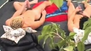 Two horny studs lie side-by-side in bed for a synchronized masturbation session