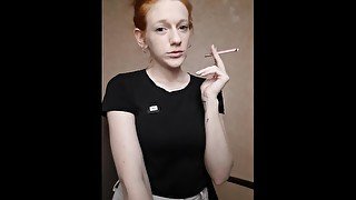 Redhead girl smokes a cigarette, hair is gathered in a bun