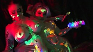 Black-light babes Nadia White and Ophelia suck off a colorful cock