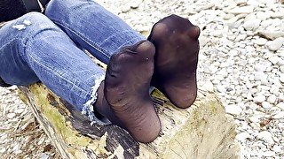 Feet In Black And Grey Nylon Socks Wiggling Toes At The Seashore