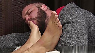 Tattooed hunk receives feet licking while masturbating