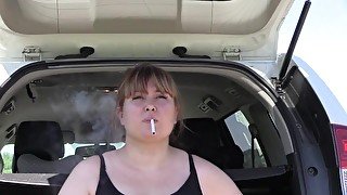 A cute bbw smokes in the street near the car