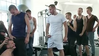 A tied up guy sucks huge dicks and get toyed in a gym