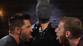 Submissive gay dude in latex abused by two guys in a dungeon