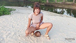 A shy girl squirts a small trickle of pee on a coconut